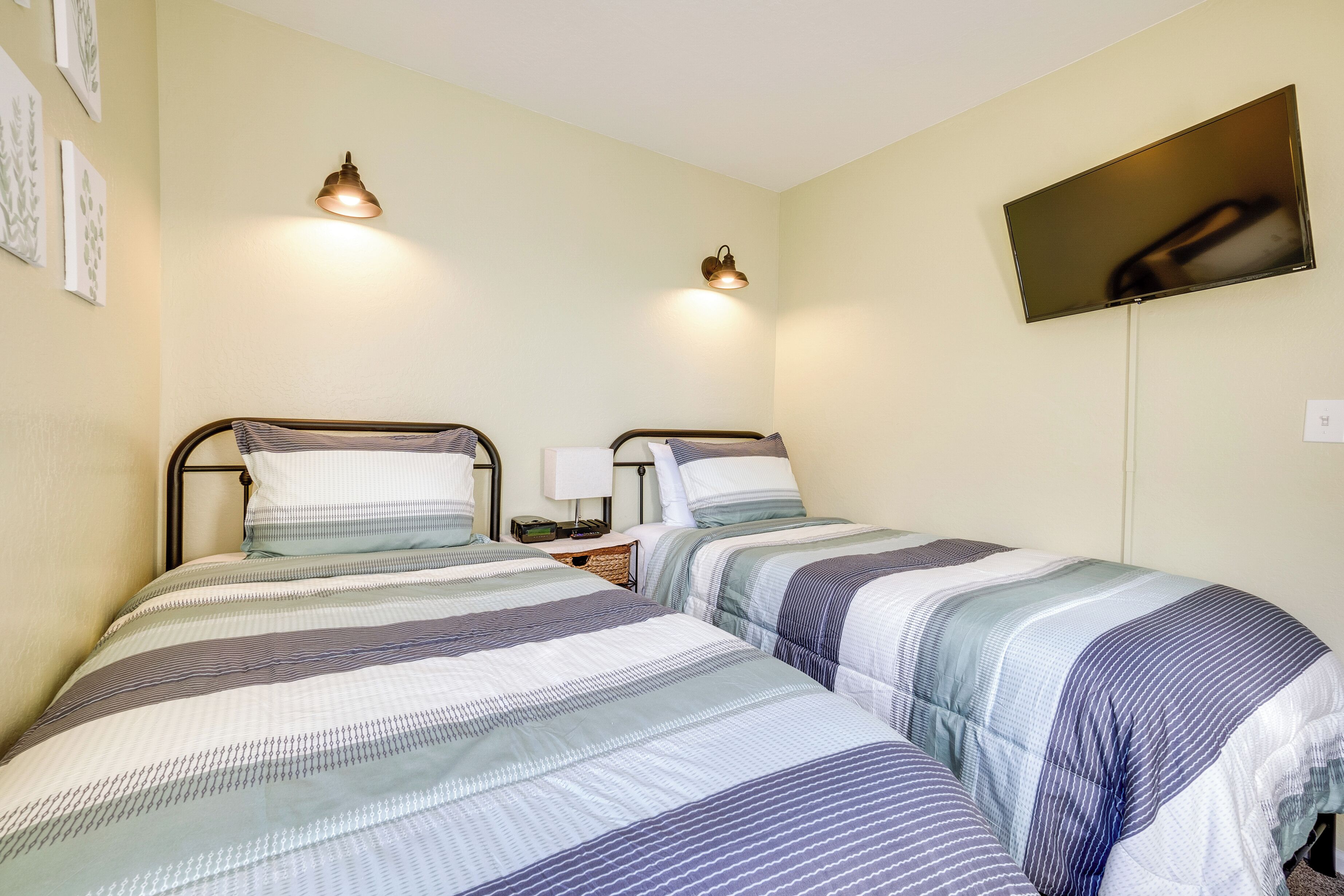 A room with two beds, each with striped bedding, a flat-screen TV mounted on the wall, and two wall-mounted lamps.