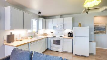 A modern kitchen with white cabinets, a microwave, stove, and refrigerator. There is a wooden countertop and a blue couch in the foreground.