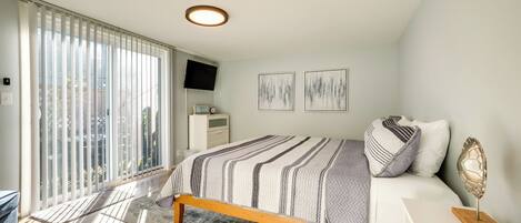 A bedroom with a bed, a bedside table, a TV, and a window with blinds.