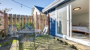 A backyard with a patio table and chairs, a wooden fence, and a sliding glass door leading to a bedroom. - Bandon Beach House Rental: Walk to Downtown! (Bandon)