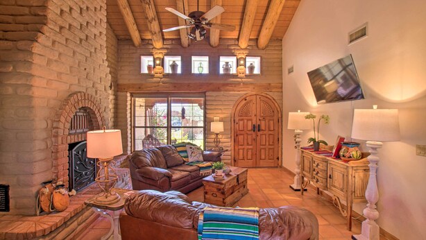 A cozy living room with a fireplace, leather sofa, wooden ceiling, and a television mounted on the wall. - Pet-friendly Cave Creek Villa w/ Backyard Oasis! (Cave Creek)