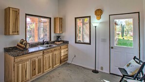 A kitchen with wooden cabinets, a granite countertop, a sink, and a coffee maker. There is a door with a window, a floor lamp, and a bench with a cushion. - Pet-friendly Cave Creek Villa w/ Backyard Oasis! (Cave Creek)