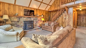 A cozy living room with a stone fireplace, wooden walls, and a staircase leading to an upper level. - Lake Harmony Access: Home w/ Game Room + Fire Pit! (Lake Harmony)