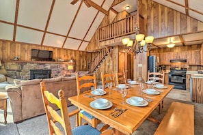 A spacious living area with a wooden dining table set for six, a stone fireplace, and a cozy sofa.