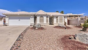 A two-story house with a garage, a front yard with rocks and a cactus, and a clear blue sky.