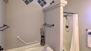 A bathroom with a bathtub, a shower, and a handrail.