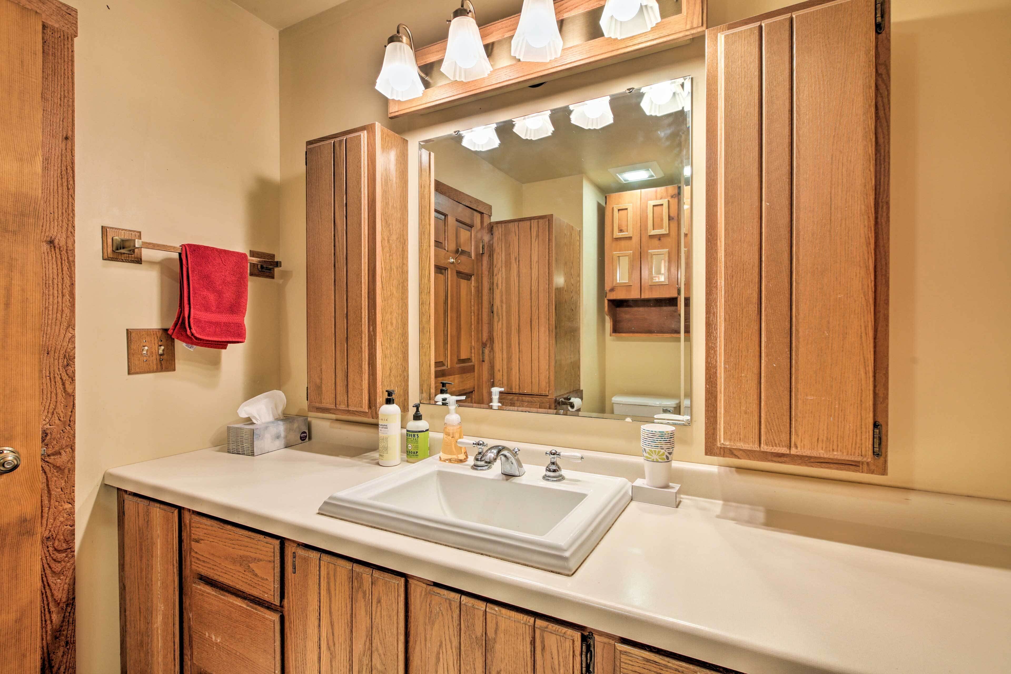 Un baño con armarios de madera, un lavabo blanco y un espejo con iluminación superior.