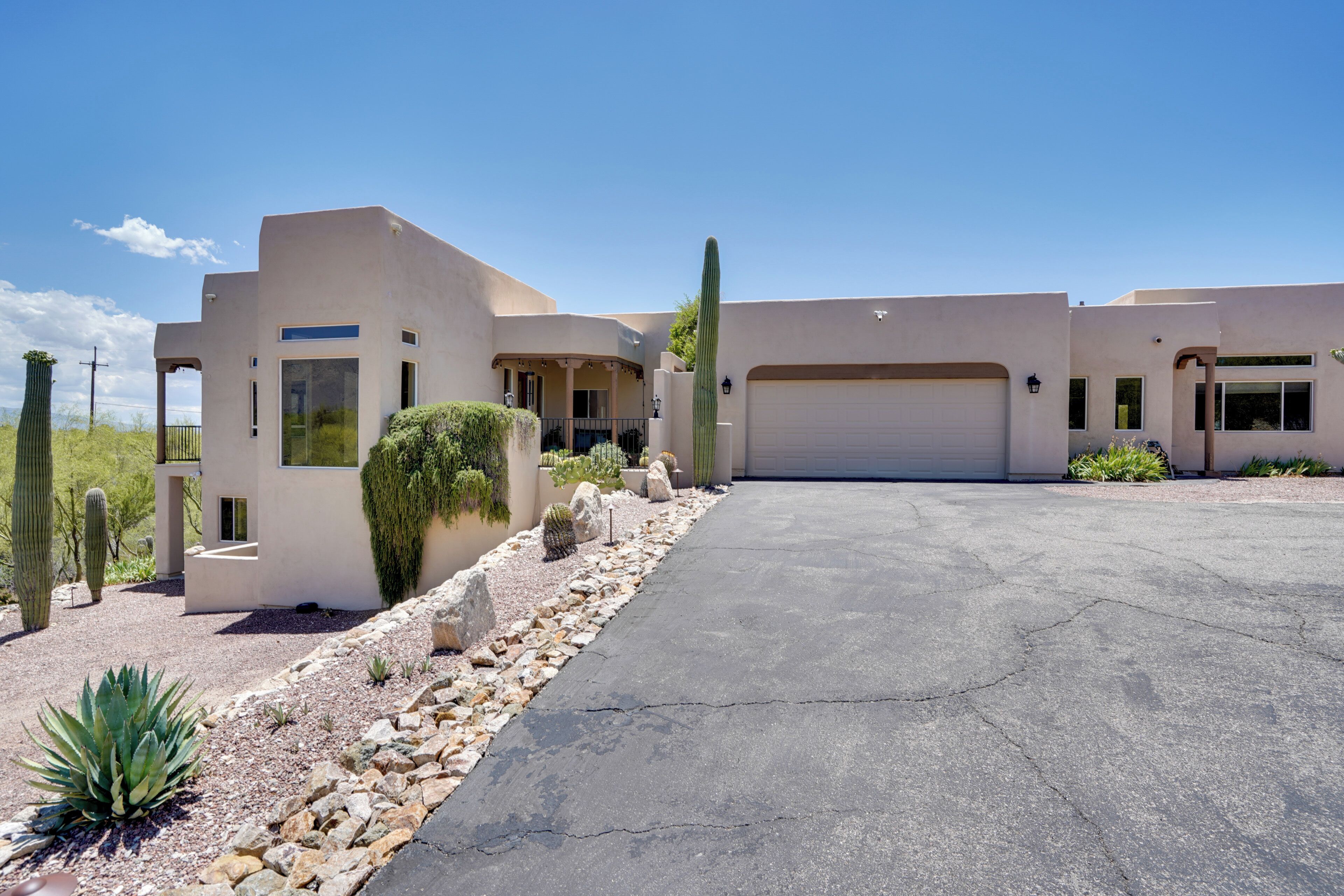 A modern two-story house with a garage, surrounded by desert landscaping including cacti and agave plants.