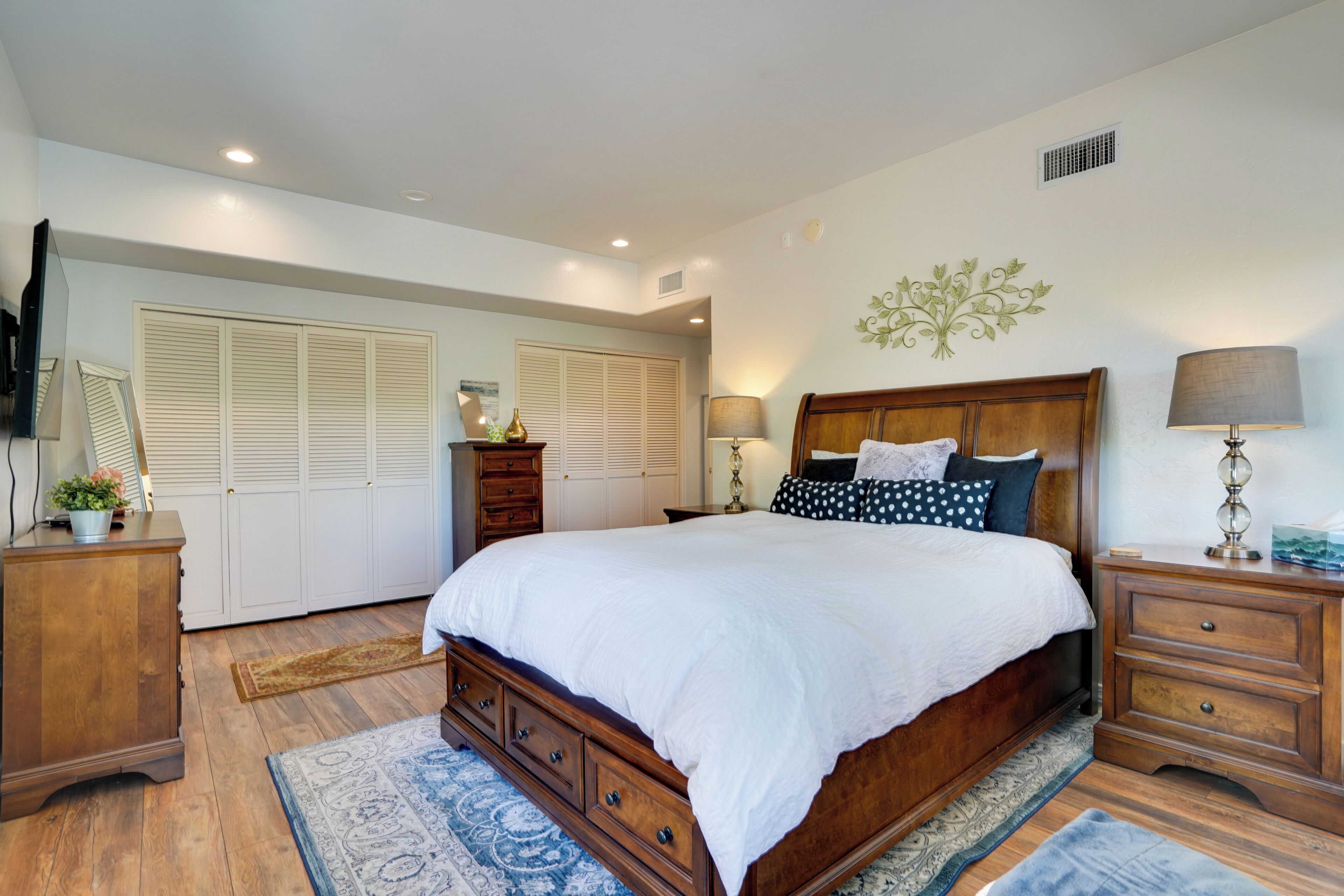 A bedroom with a large bed, wooden dresser, nightstand, and a mirror.