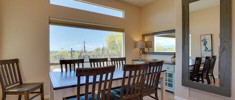 A dining area with a large table and chairs, a window with a view of the outdoors, and a large mirror on the wall.