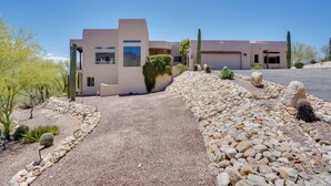 Una casa moderna con vialetto sterrato, circondata da cactus e rocce.