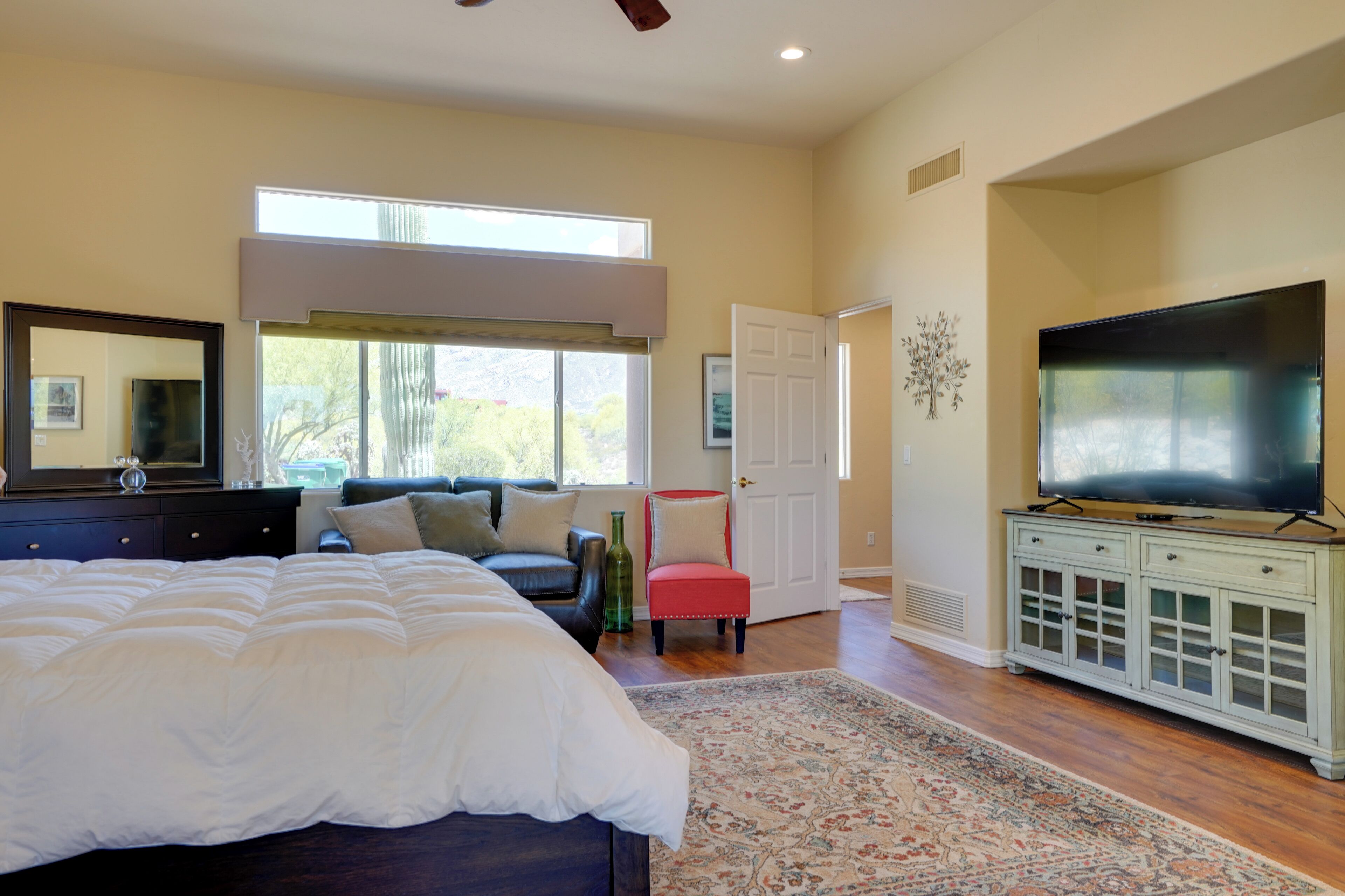 A bedroom with a large bed, a television, and a window with a view of trees.