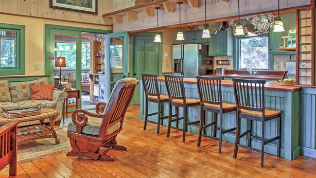 A rustic interior with wooden floors, a dining area with bar stools, a rocking chair, and a kitchen area with a refrigerator and sink. - Waterfront Denmark Complex w/ Dock on 12 Acres! (Denmark)