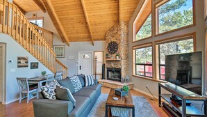 A spacious living room with a stone fireplace, wooden ceiling, large windows, and a staircase. - Modern Mountain Chalet: Munds Park Retreat w/ Deck (Munds Park)