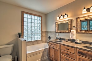 Une salle de bain avec une baignoire, un meuble-lavabo en bois et une grande fenêtre avec du verre dépoli.