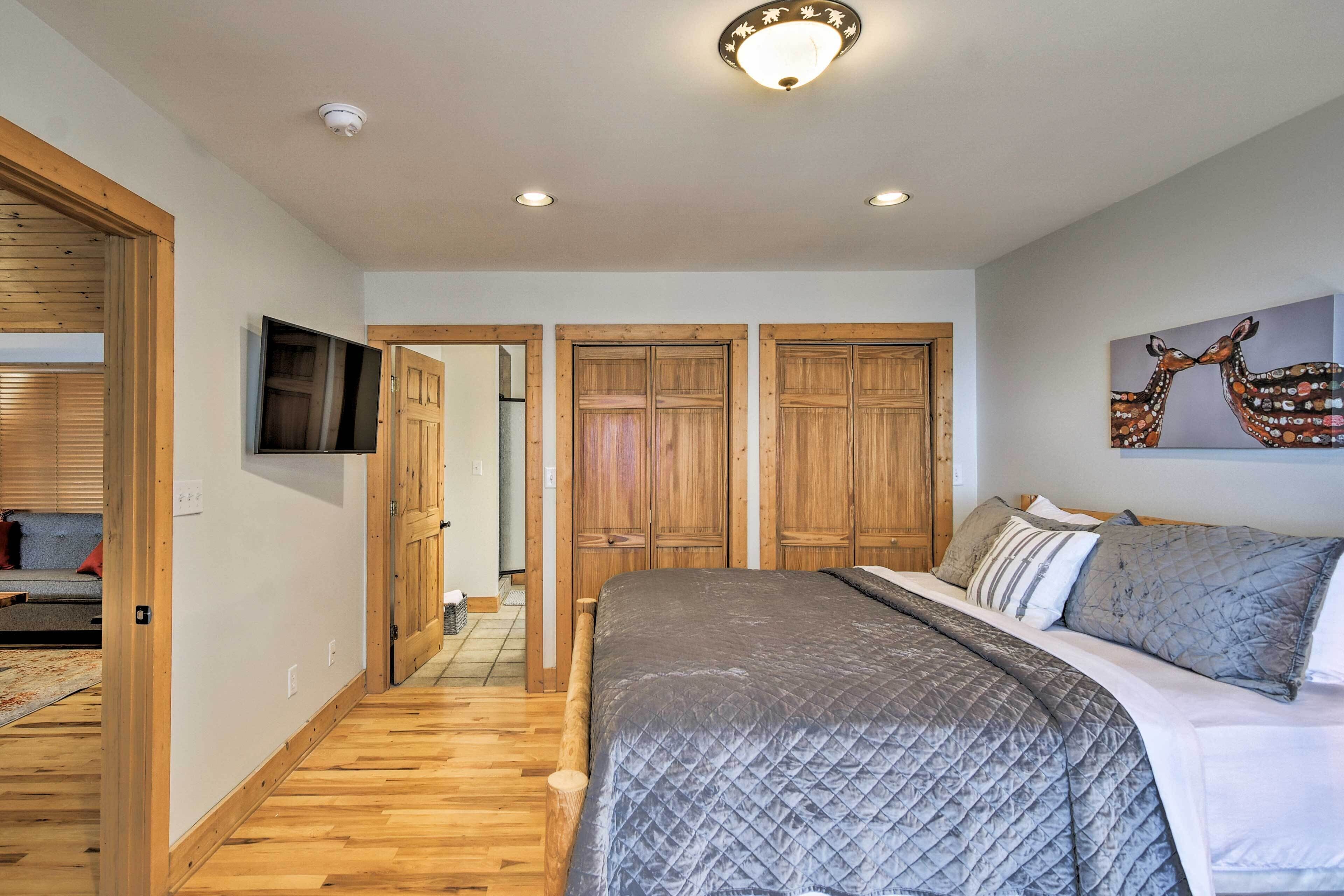 A bedroom with a large bed, wooden wardrobe, and a television on the wall.