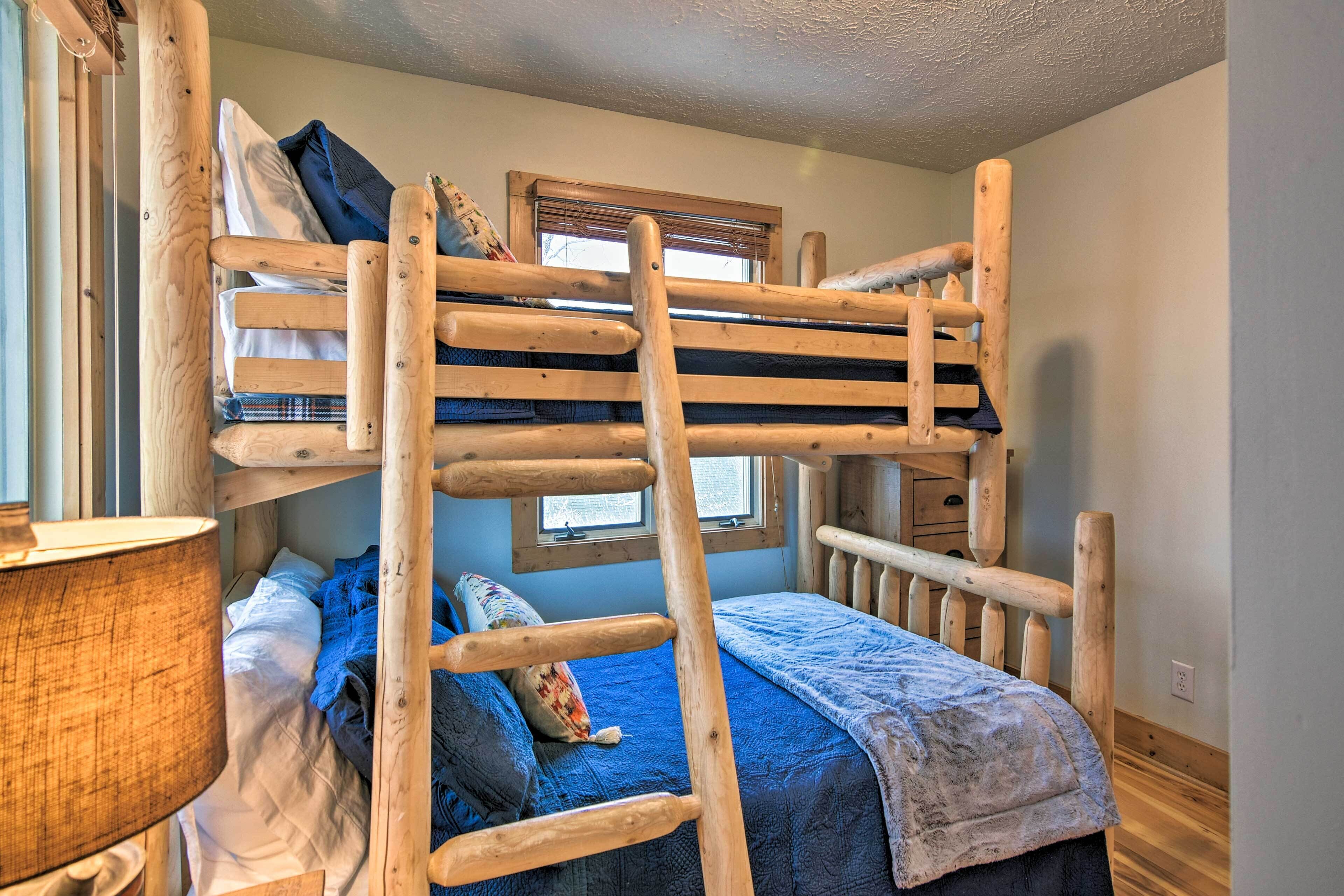 A bunk bed with a wooden ladder, a window with blinds, a lamp, and a blue blanket.