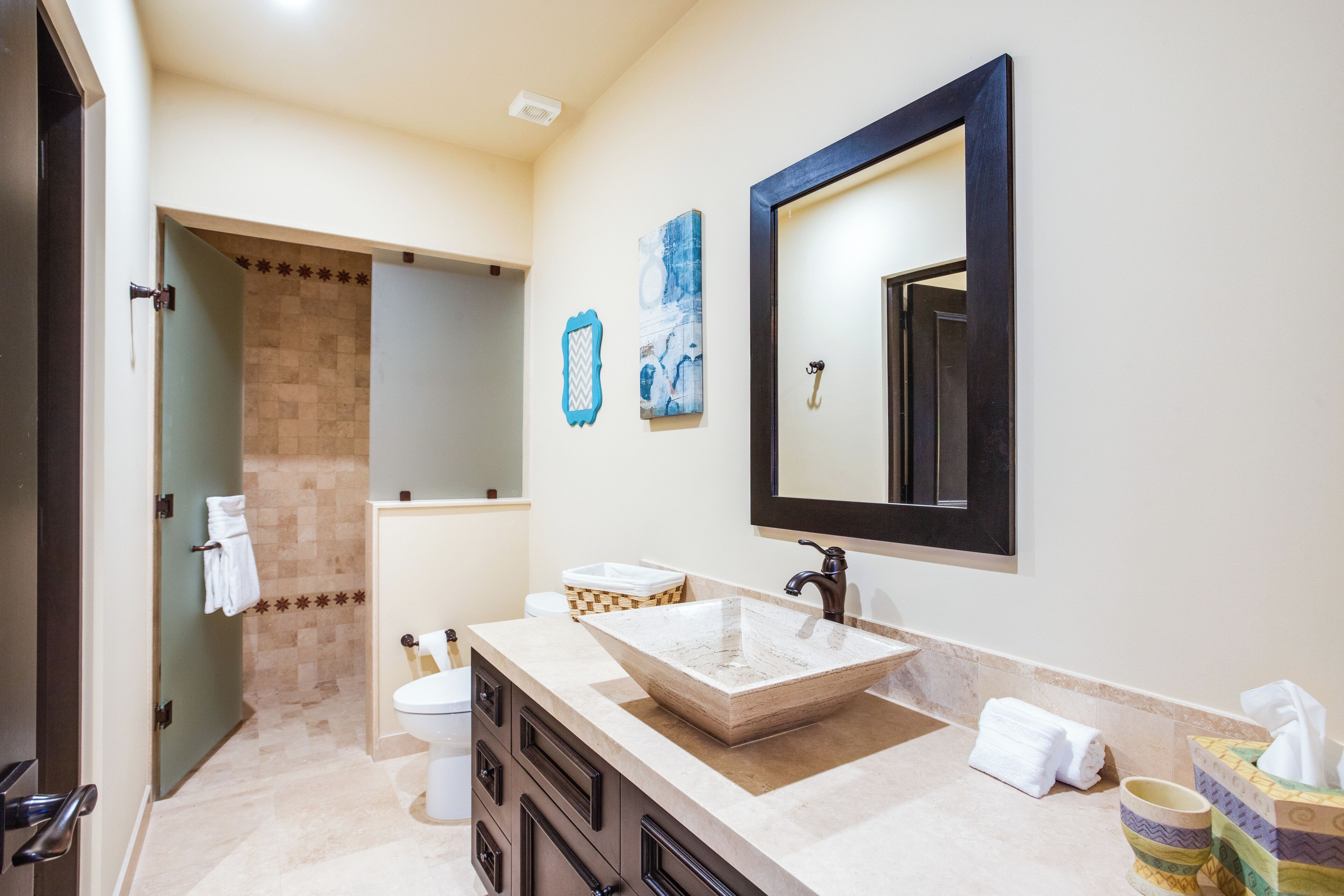 A bathroom with a large sink, a mirror, and a toilet. There are towels hanging on the wall and a basket on the counter.