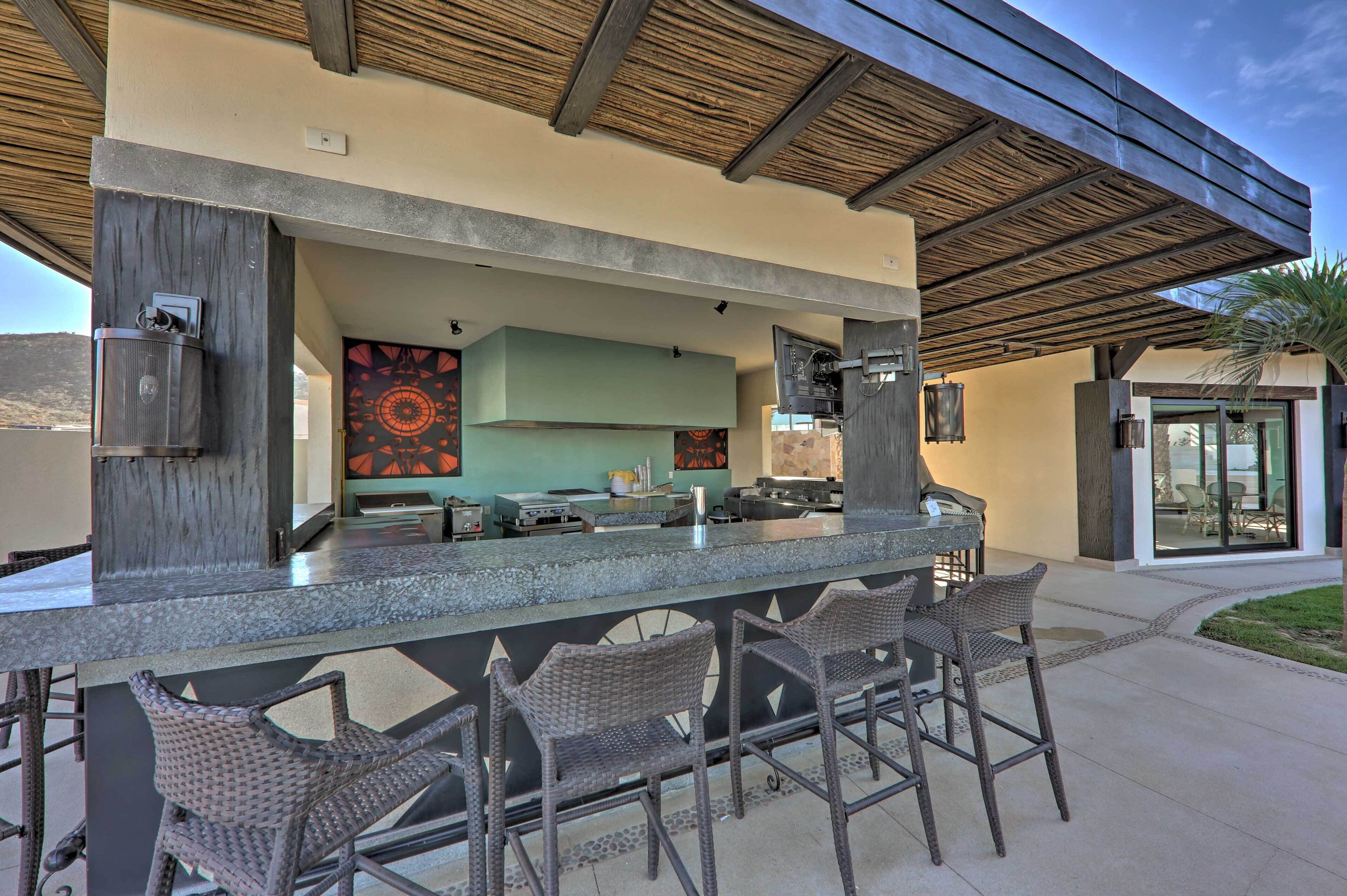 An outdoor bar area with a counter, bar stools, and a kitchen in the background.