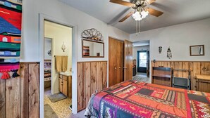 Un dormitorio con un armario de madera, una cama con colcha colorida, un ventilador de techo y un espejo en la pared.