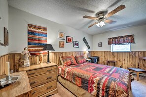 A bedroom with a wooden headboard, a large bed with a patterned bedspread, a ceiling fan, and a window with a view of the outdoors. - Cabin w/ Deck 3 Mi to Ski Cloudcroft & Hiking (Cloudcroft)