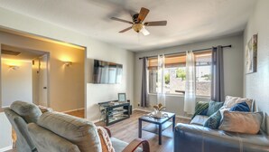 A living room with a ceiling fan, a flat-screen TV, a glass coffee table, and a sofa with cushions. - Phoenix Home w/ Pool, Near Golf, Hiking & More! (Phoenix)