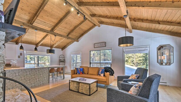 Ein geräumiger Wohnbereich mit hohen Decken, Holzbalken, einer Couch, einem Couchtisch und Blick ins Freie.