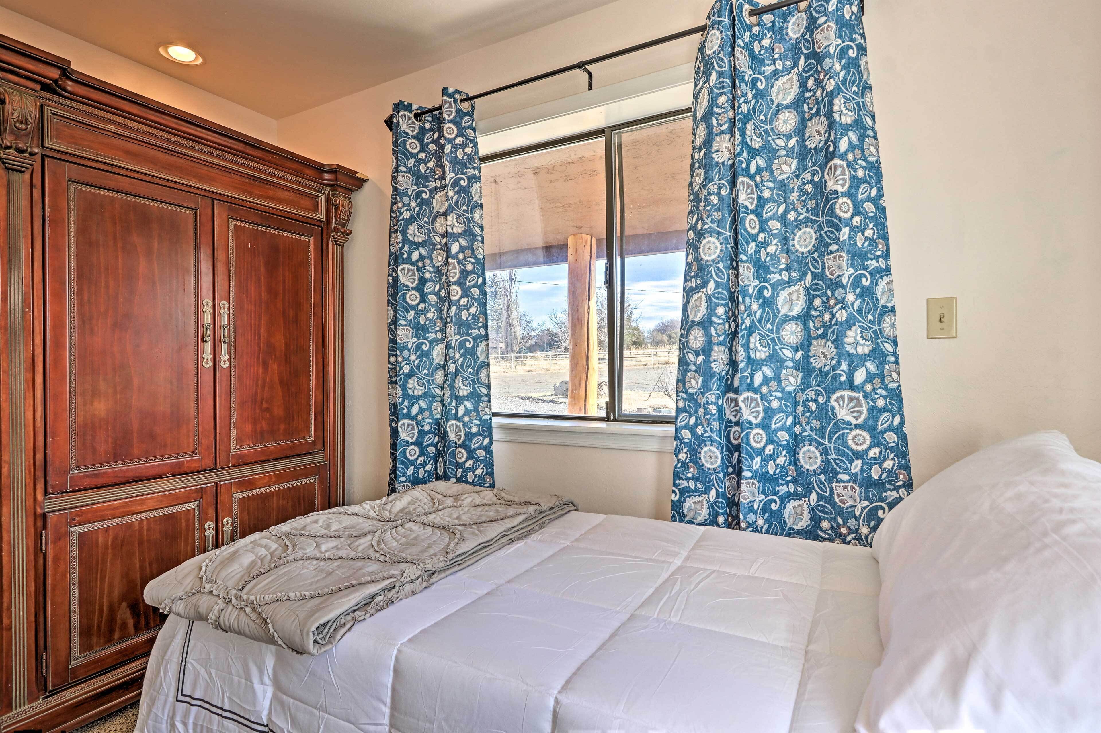 A bedroom with a large wooden wardrobe, a bed with a white comforter, and blue floral curtains.