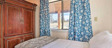 A bedroom with a large wooden wardrobe, a bed with a white comforter, and blue floral curtains.