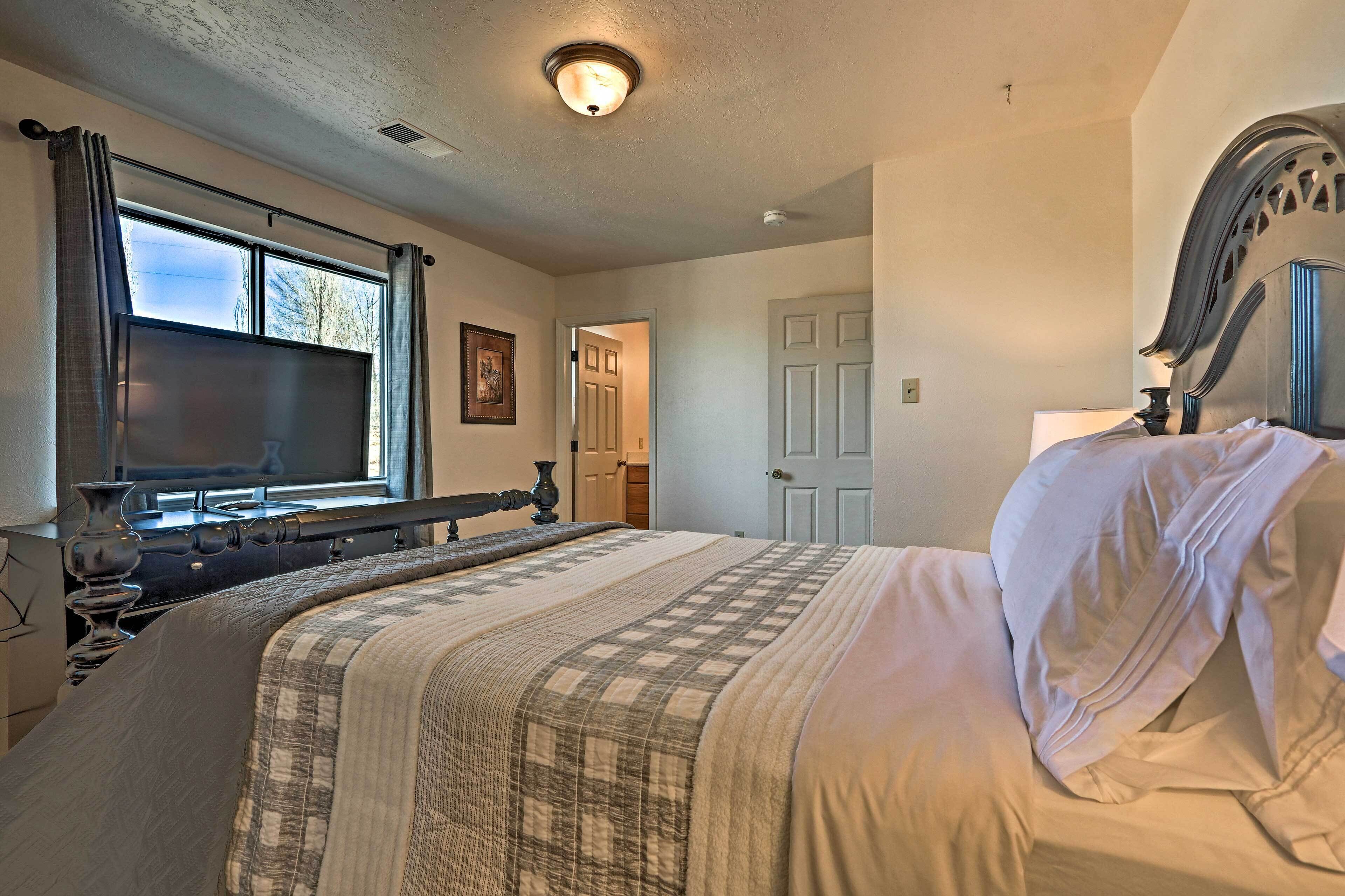 A bedroom with a large bed, a window with curtains, a door, and a ceiling light.