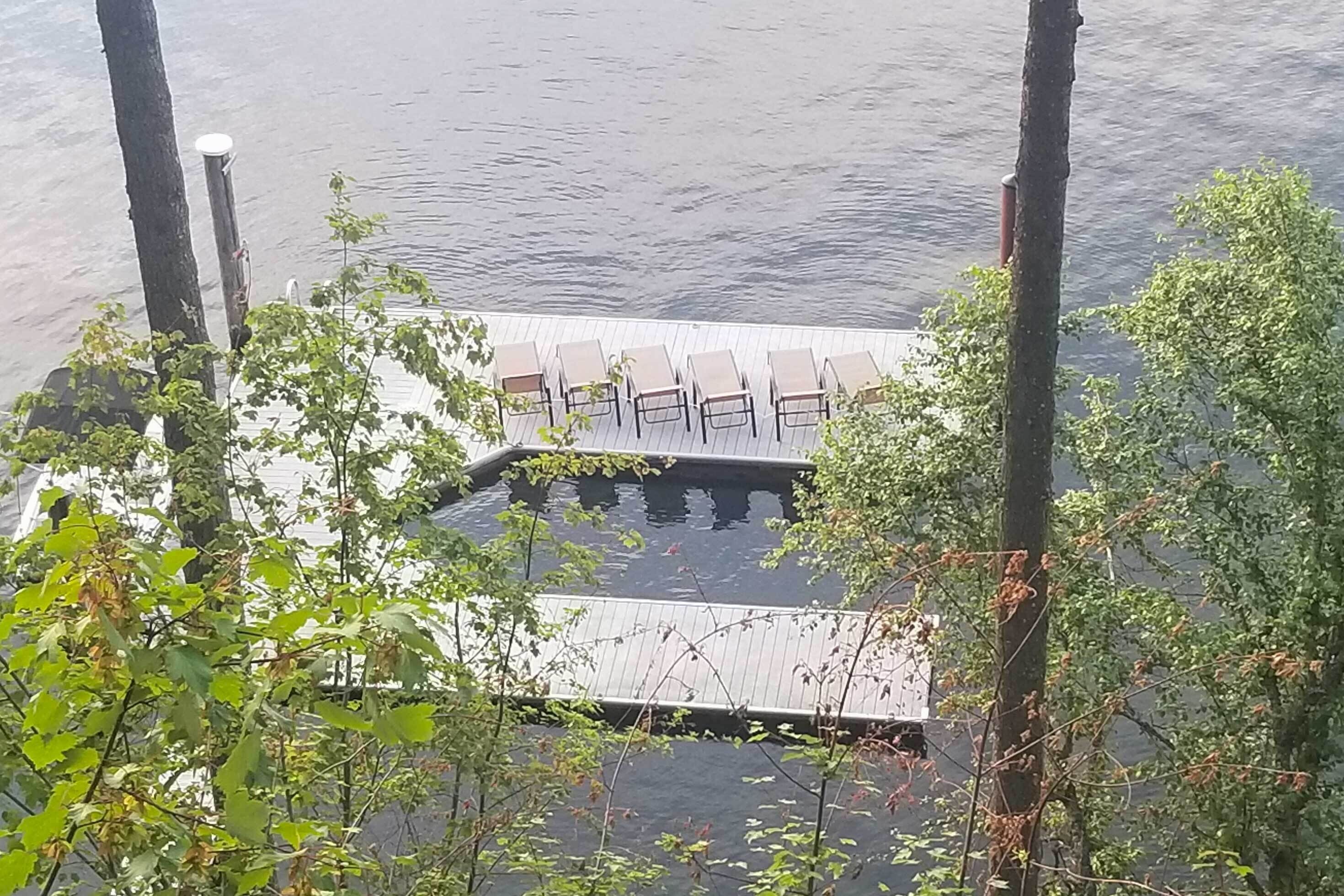 A dock with chairs and a small wooden platform over water, surrounded by trees.