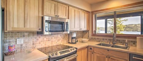 A kitchen with wooden cabinets, stainless steel appliances, a window with a view, and a tiled backsplash.