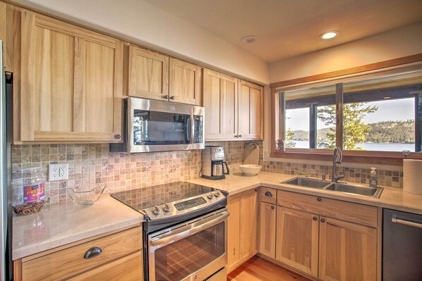 A kitchen with wooden cabinets, stainless steel appliances, a window with a view, and a tiled backsplash.