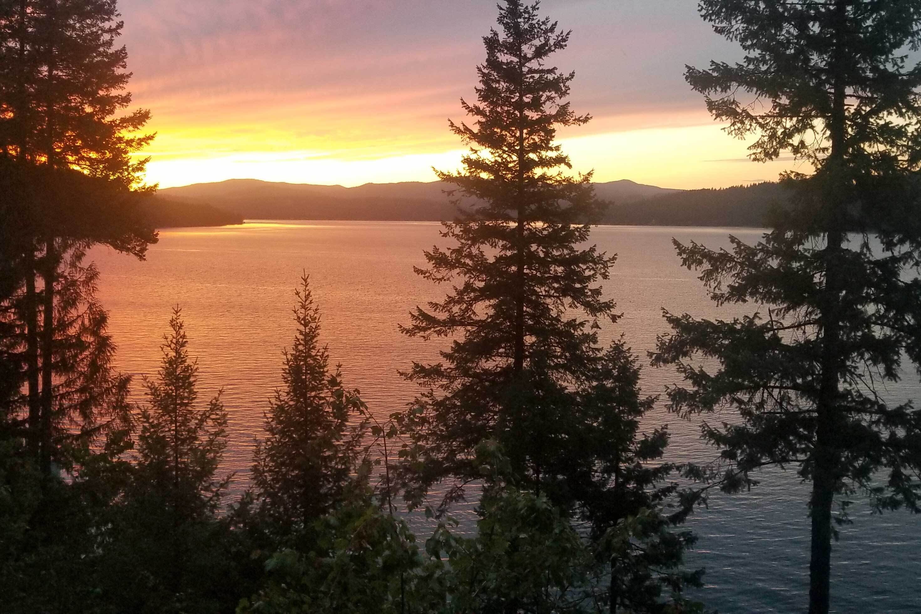 A serene lake at sunset with trees framing the view.