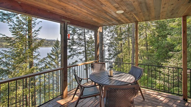 A wooden deck with a table and chairs overlooking a lake and forest. - Swim, Boat & Explore! South Lake Coeur D'alene Gem (Worley)
