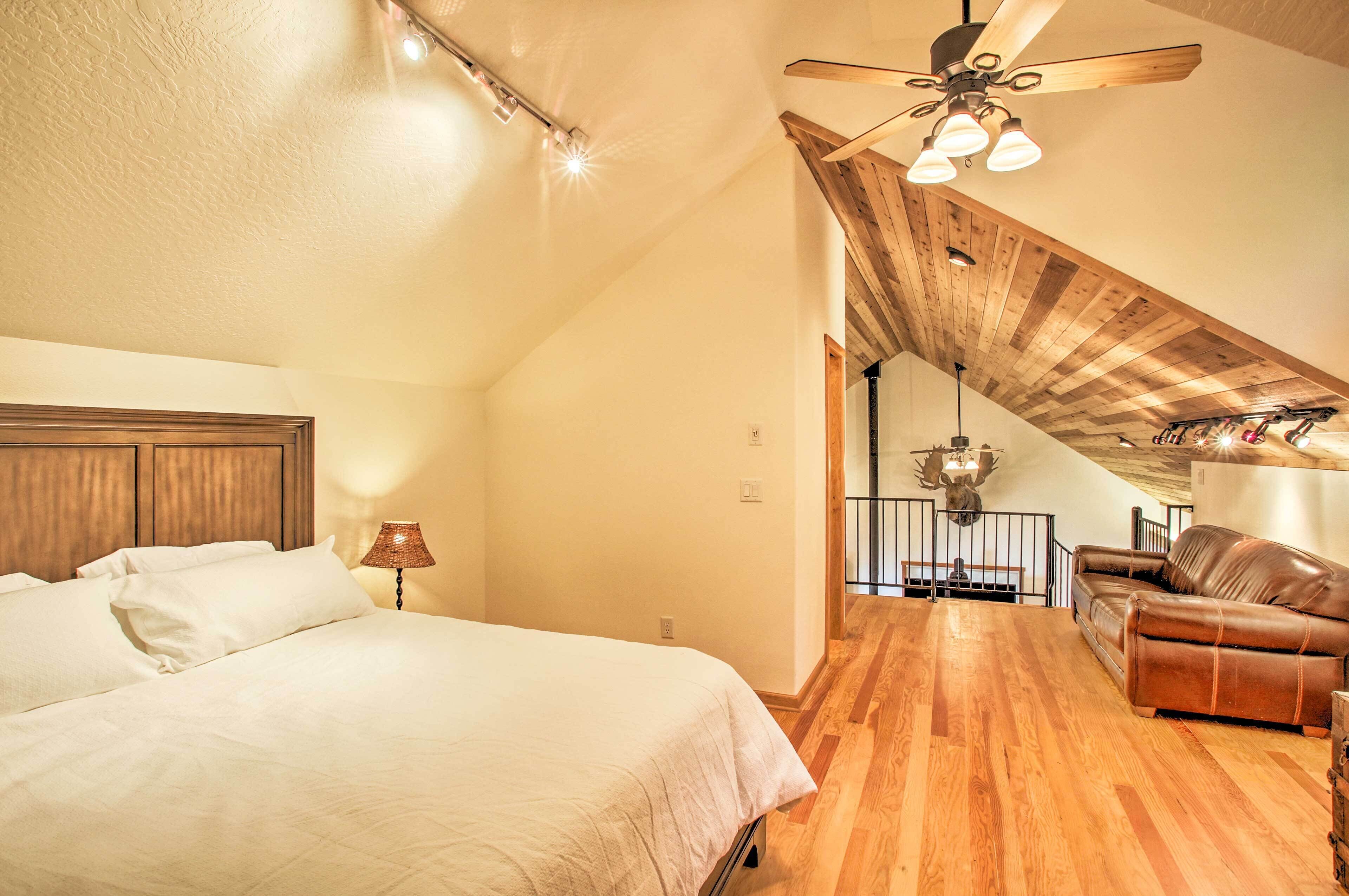 A bedroom with a bed, a ceiling fan, and a staircase leading to a loft area with a leather sofa.