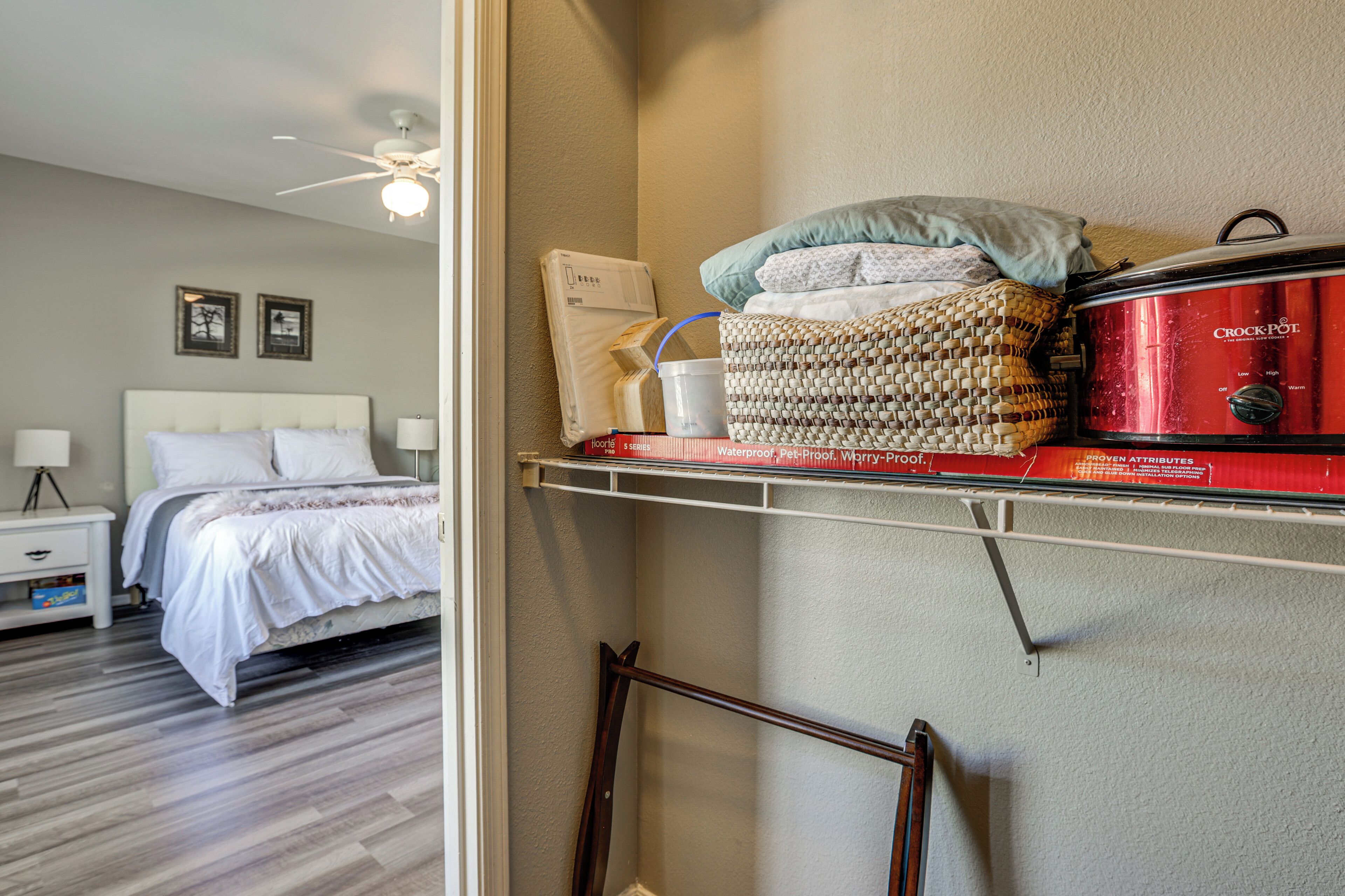 A bedroom with a bed, nightstand, and a shelf with a Crock-Pot and other items.