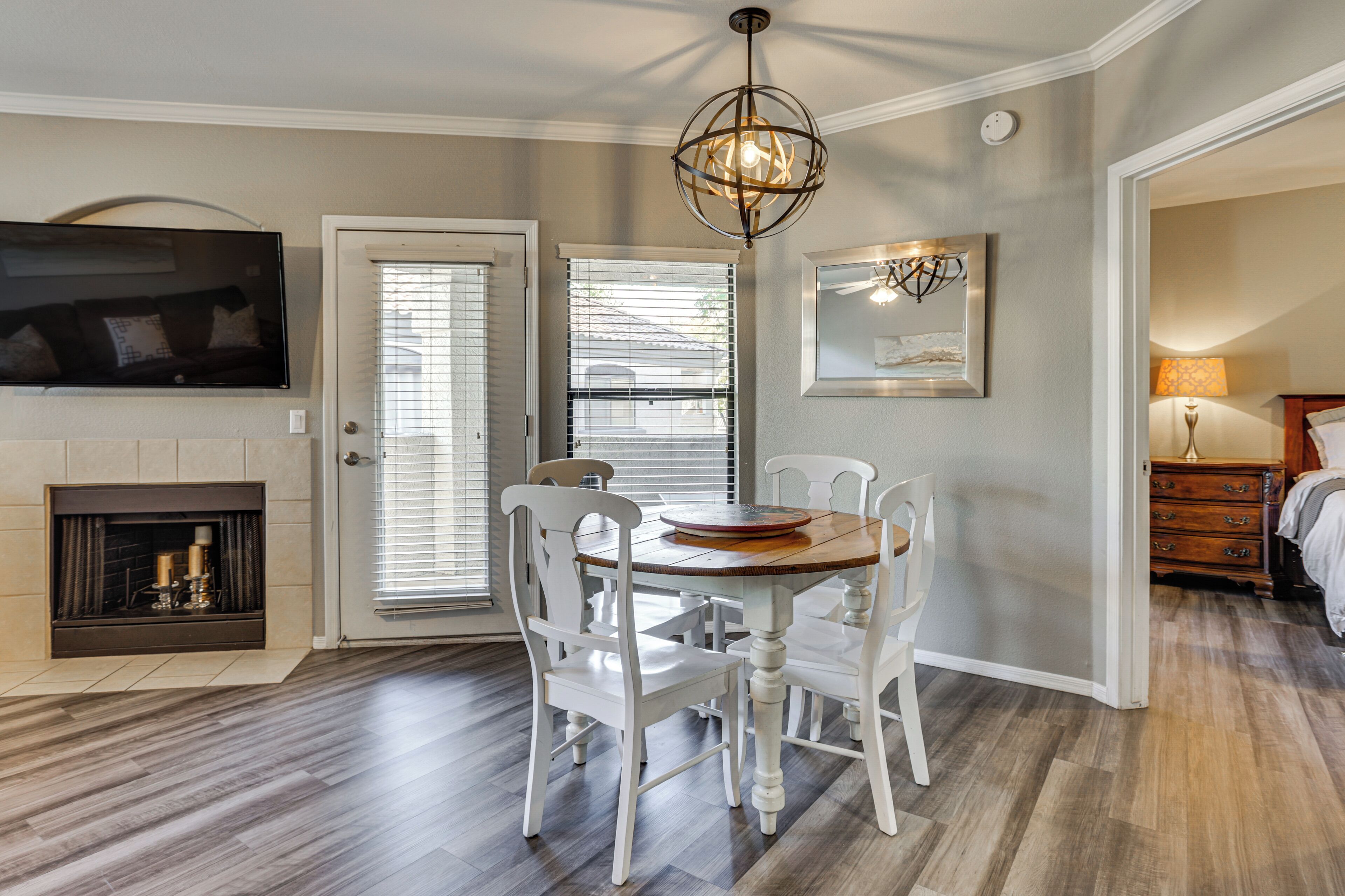 A dining area with a wooden table and white chairs, a fireplace, a television mounted on the wall, and a ceiling light fixture.