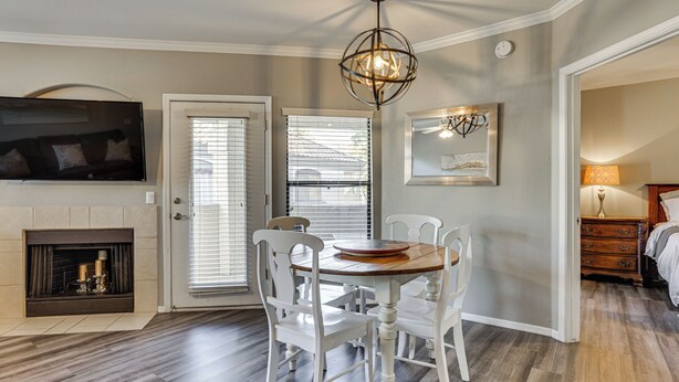 A dining area with a wooden table and white chairs, a fireplace, a television mounted on the wall, and a ceiling light fixture. - Close to Golfing & Shopping: Condo in Scottsdale! (Scottsdale)