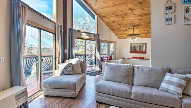 A spacious living room with a large window, a wooden ceiling, and a cozy seating area. - Pet-friendly Gilford Home by Gunstock Ski Mountain (Gilford)