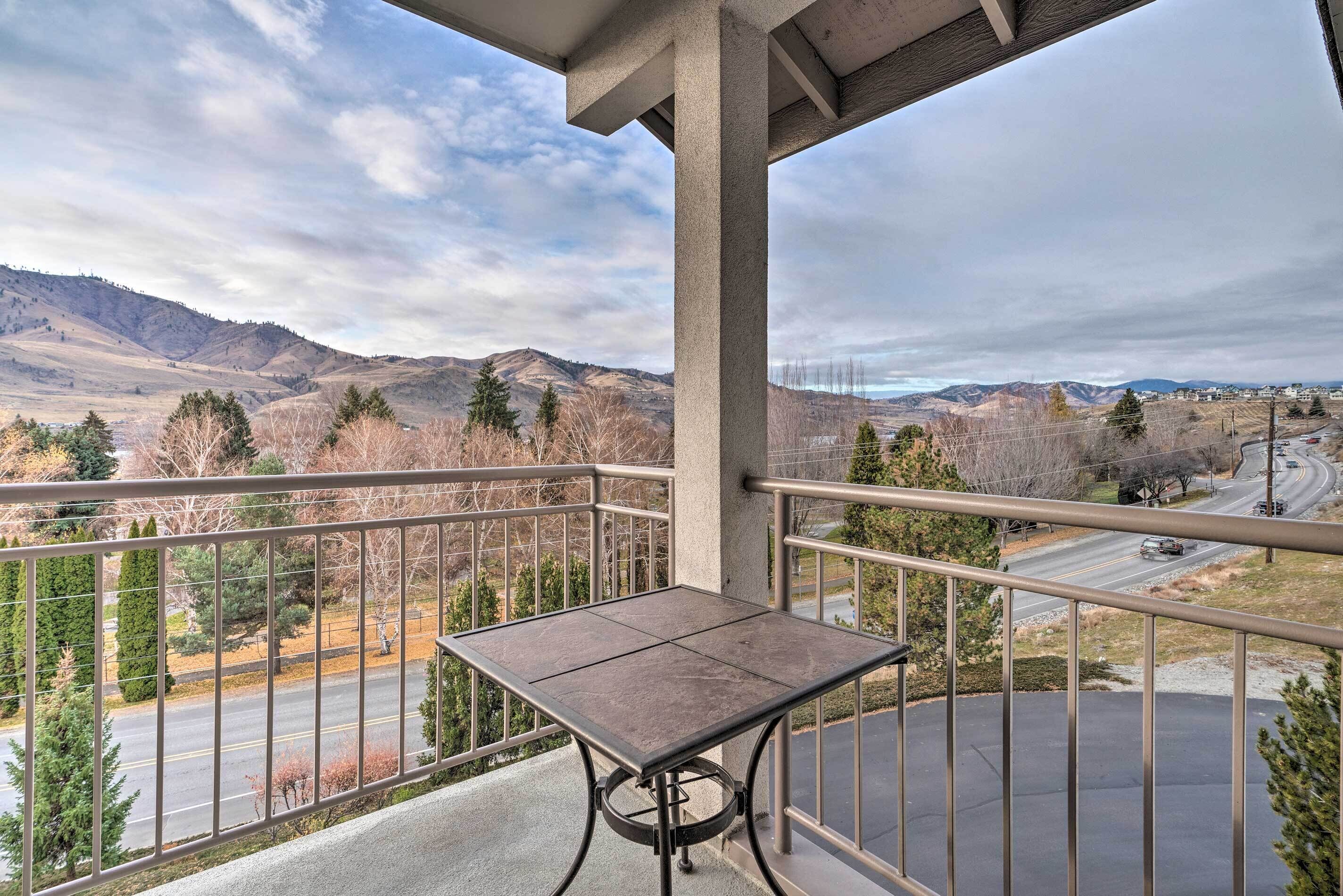 Een balkon met een tafel en uitzicht op een weg en bergen.