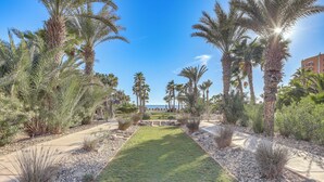 A landscaped pathway with palm trees and a view of a building in the distance. - Beachfront Rocky Point Villa w/ Ocean Views! (Puerto Peñasco)