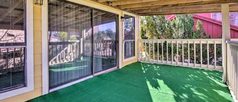 Un patio techado con piso de césped artificial verde, grandes puertas correderas de vidrio y una valla blanca.