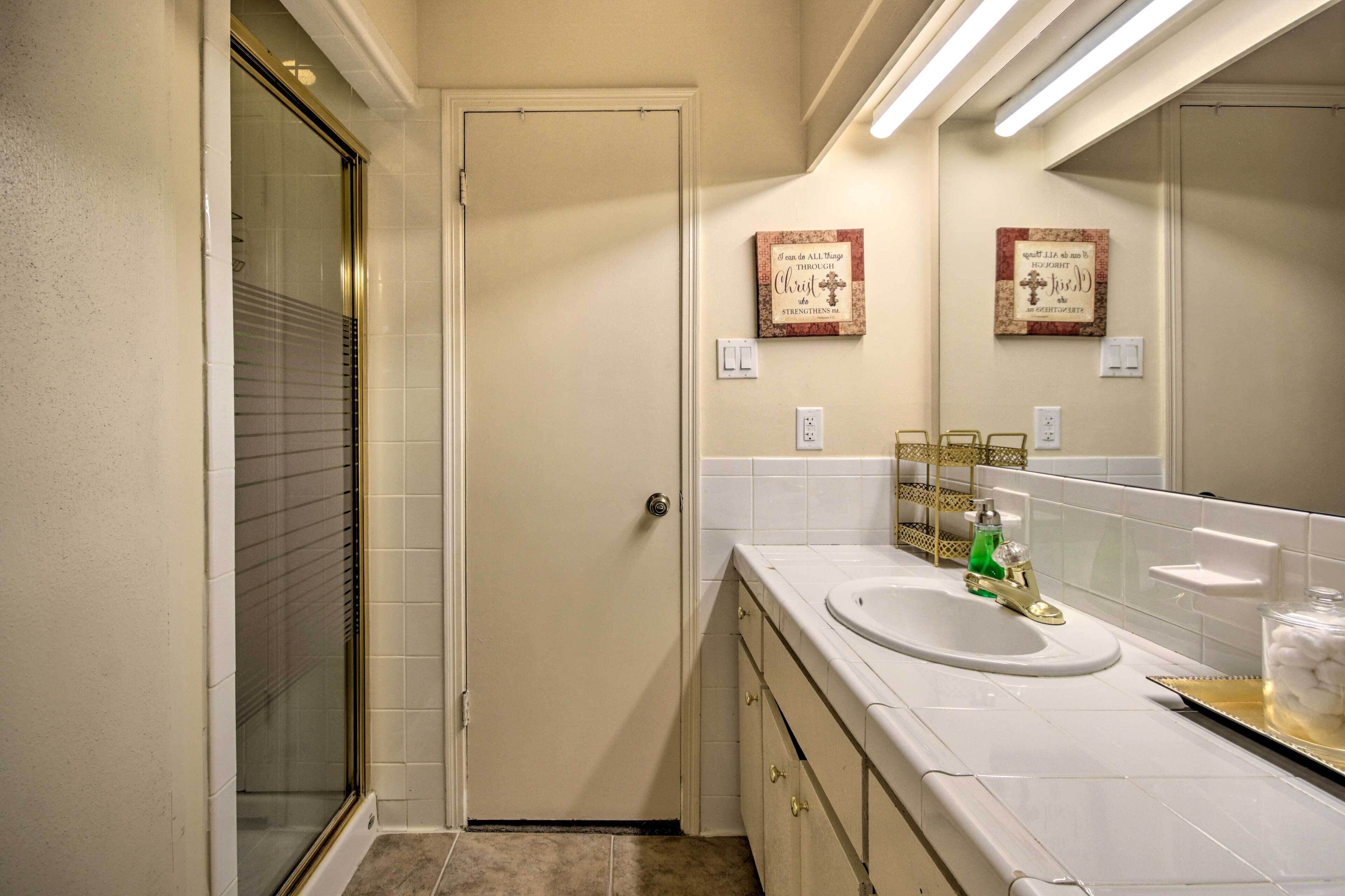 A bathroom with a shower, a sink with a gold faucet, and two wall-mounted light switches.