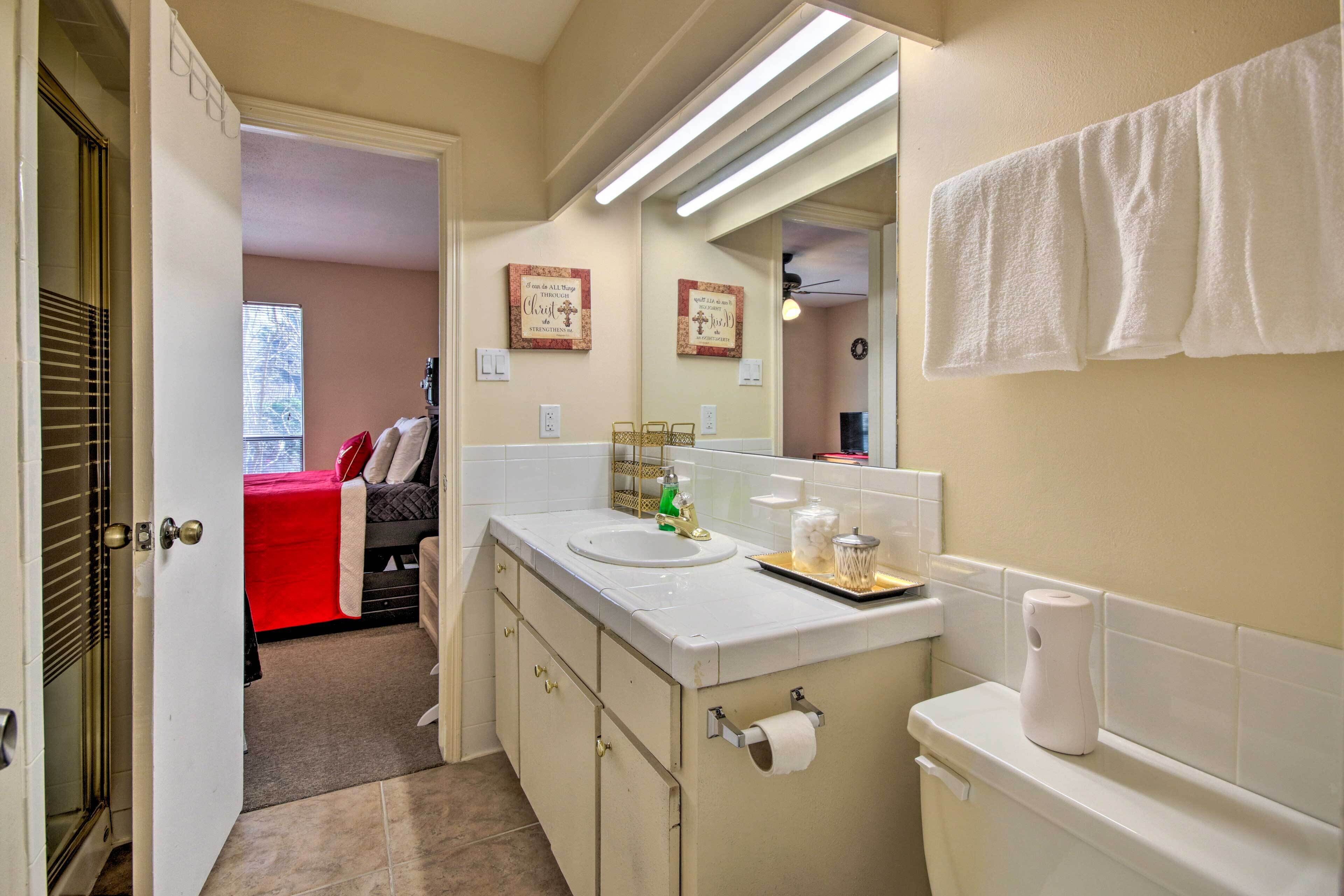 A bathroom with a white sink, toilet, and towel hanging on the wall. There is a mirror above the sink and a window in the background.