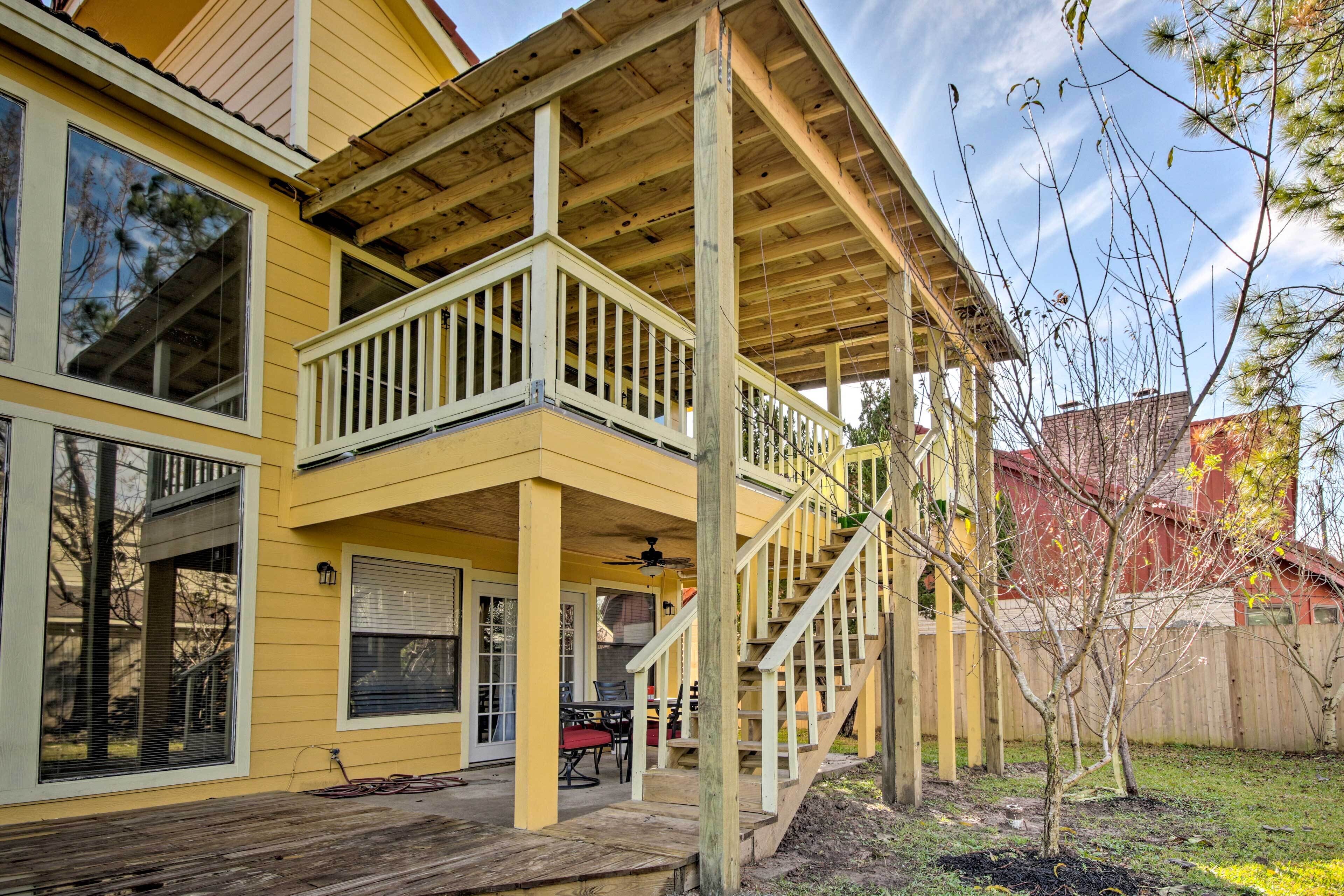 A yellow two-story house with a covered porch, a staircase, and a small patio area with outdoor furniture.