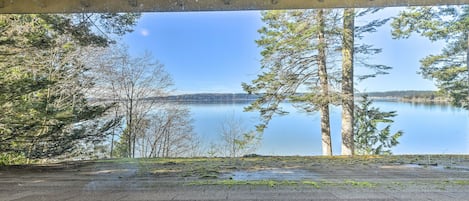 A view from under a wooden structure overlooking a calm lake surrounded by trees.