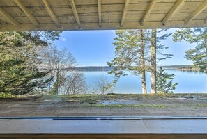 Une vue prise depuis l’intérieur d’une structure en bois surplombant un lac paisible, entouré d’arbres.