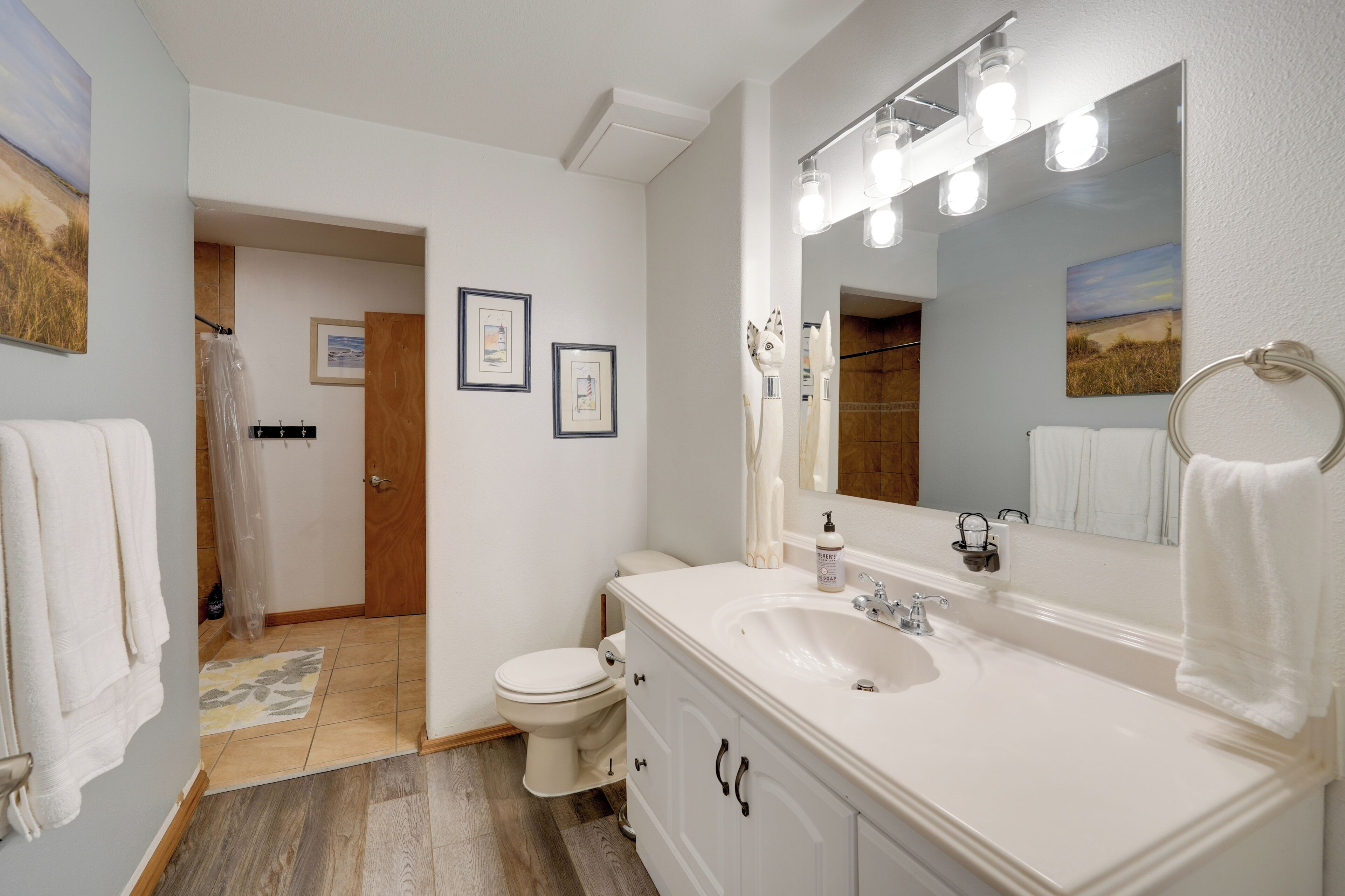 A bathroom with a white sink, mirror, and toilet. There are framed pictures on the wall and a shower curtain.