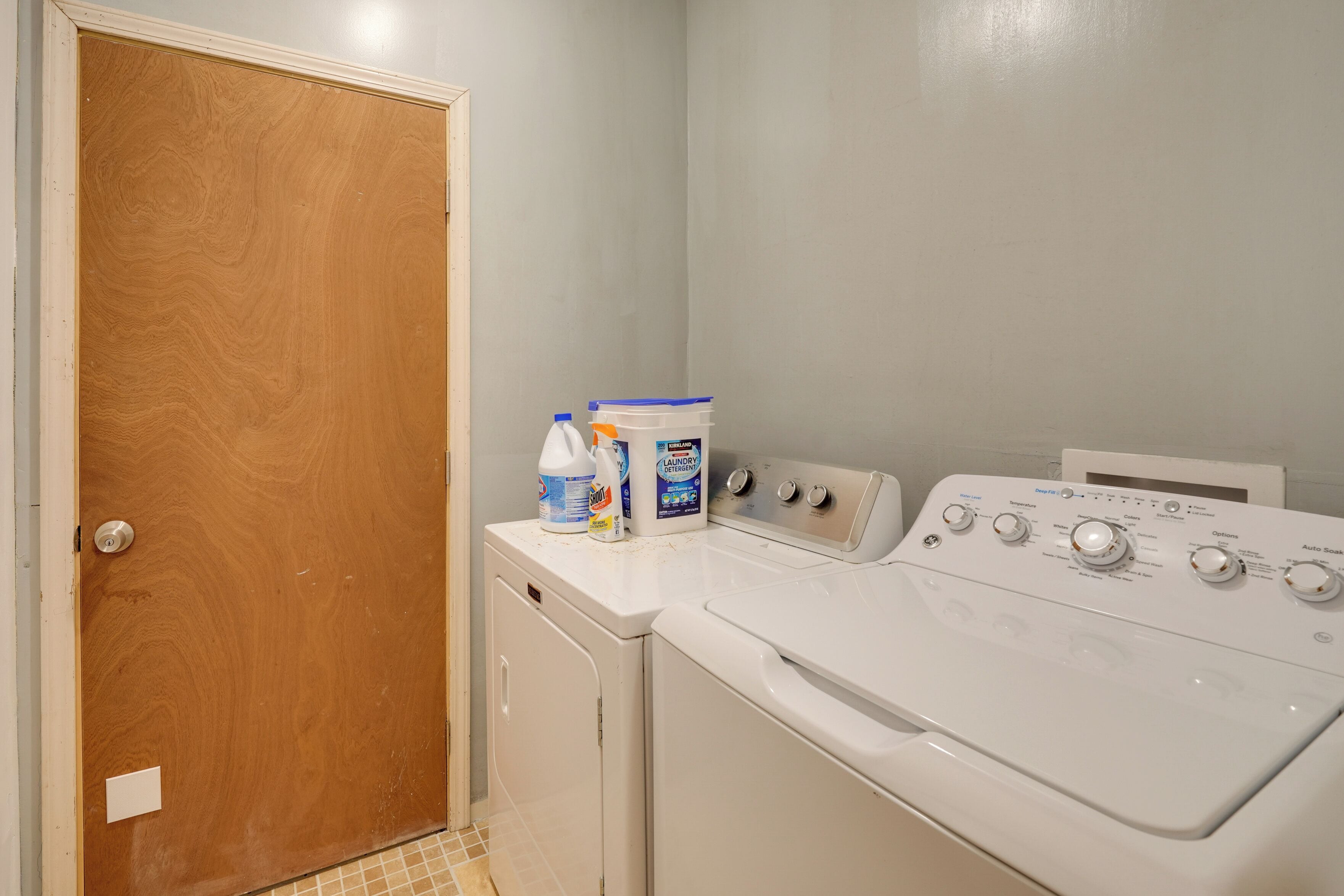 A laundry room with a wooden door, a washing machine, and detergent bottles.